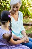 Smiling grandmother holding hands of granddaughter while sitting on bench