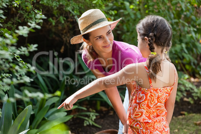 Smiling mother looking at girl pointing by plants