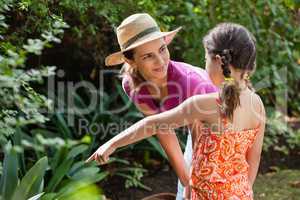 Smiling mother looking at girl pointing by plants