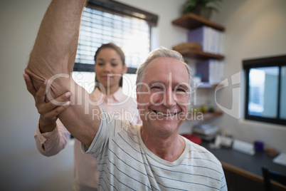 Smiling senior man looking away while female doctor examining elbow