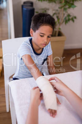 Boy looking at female therapist wrapping bandage on hand
