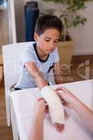 Boy looking at female therapist wrapping bandage on hand