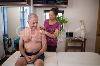 Female therapist applying elastic therapeutic tape on shoulder of shirtless senior male patient