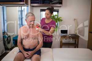 Female therapist applying elastic therapeutic tape on shoulder of shirtless senior male patient