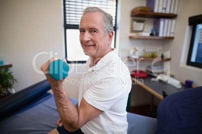 Side view portrait of smiling senior male patient lifting dumbbell