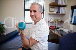 Side view portrait of smiling senior male patient lifting dumbbell