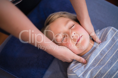 Boy lying with eyes closed receiving neck massage from female therapist