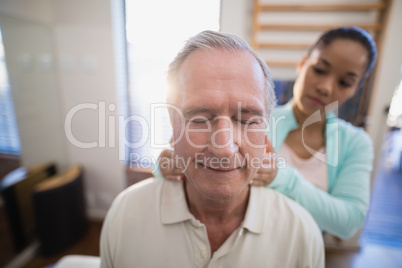 Senior male patient with eyes closed receiving neck massage from female therapist