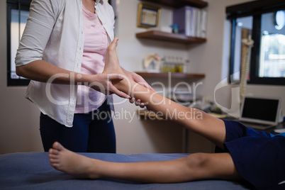 Young female therapist massaging sole of foot with boy on bed