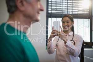 Smiling female therapist photographing senior male patient against window