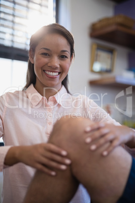Portrait of smiling female therapist examining knee with senior male patient