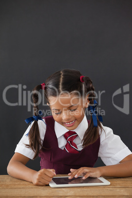 Schoolgirl using digital tablet against blackboard