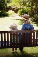 Rear view of granddaughter and grandmother wearing hats sitting on wooden bench