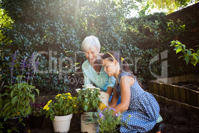 Grandmother looking at girl planting flower pots
