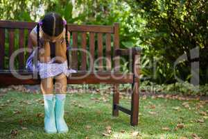 Depressed girl sitting on wooden bench with head in hands
