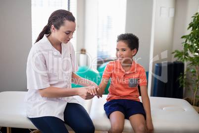 Female therapist examining hand of boy while sitting on bed