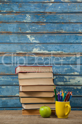 Book stack, color pencils and apple on wooden table