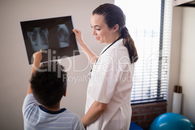 Female therapist looking at boy pointing towards x-ray against wall