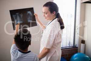 Female therapist looking at boy pointing towards x-ray against wall