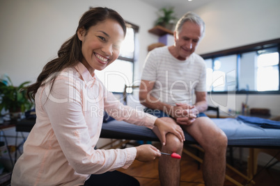 Portrait of female therapist examining knee of senior male patient with reflex hammer