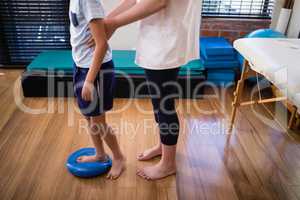 Low section female therapist holding boy standing on blue stress ball