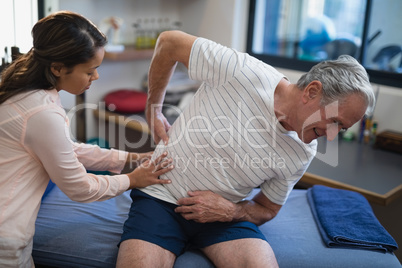 Female therapist examining back of senior male patient sitting on bed