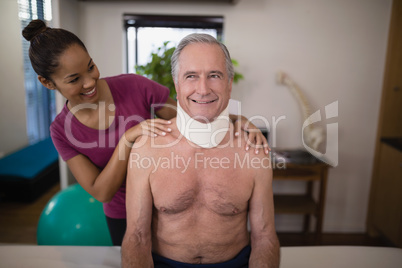 Smiling female therapist looking at senior male patient with neck collar
