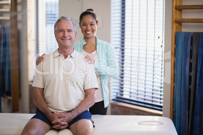 Portrait of smiling young female physiotherapist standing by male patient sitting on bed