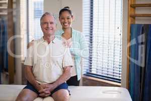 Portrait of smiling young female physiotherapist standing by male patient sitting on bed