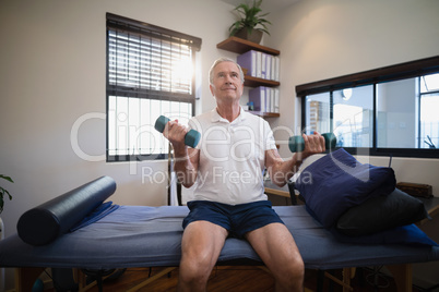 Senior male patient lifting dumbbells while sitting on bed