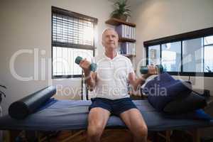Senior male patient lifting dumbbells while sitting on bed