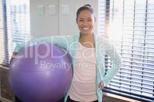 Portrait of smiling young female physiotherapist holding purple exercise ball