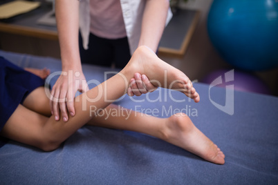 Female physiotherapist examining leg of boy lying on bed