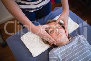High angle view of boy with eyes closed receiving head massage from female physiotherapist