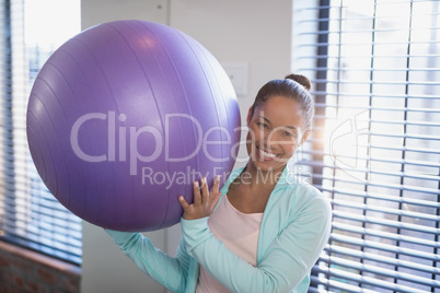 Portrait of smiling young female doctor holding purple exercise ball