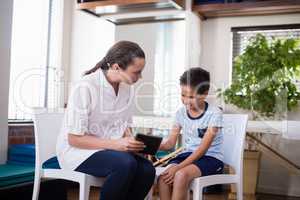 Female therapist looking at boy while using digital tablet