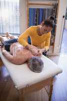 High angle view of shirtless senior male patient lying on bed receiving neck massage from female the