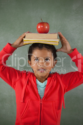 Young girl balancing books and apple on her head