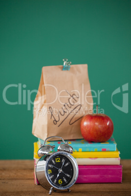 Alarm clock and lunch paper bag with apple on books stack