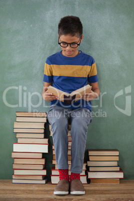 Schoolboy sitting on books stack and reading book