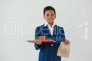 Schoolboy holding apple, books and disposable lunch bag against white background