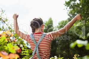 Rear view of girl standing with arms raised amidst plants against sky