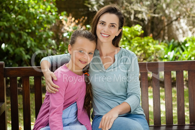 Portrait of smiling woman and daughter sitting on wooden bench