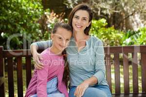 Portrait of smiling woman and daughter sitting on wooden bench