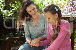 Mother looking at girl while holding hands on wooden bench
