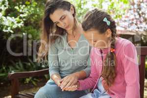 Mother and daughter looking down while holding hands on wooden bench