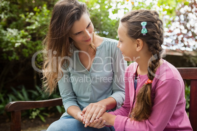 Smiling mother holding hands of daughter while sitting on wooden bench