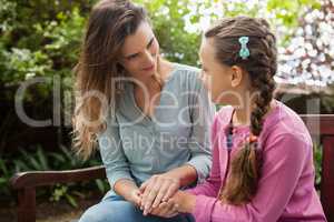 Smiling mother holding hands of daughter while sitting on wooden bench