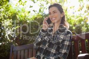 Low angle view of smiling beautiful woman talking on mobile phone while sitting on wooden bench