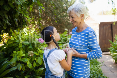 Smiling senior woman holding hands of granddaughter while standing against plants